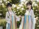 A couple of women standing next to each other in front of flowers.