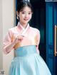 A woman in a blue and pink hanbok poses for a picture.