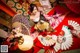 A woman in a kimono sitting on a red carpet surrounded by fans.