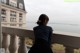 A woman sitting on a balcony looking out over the water.